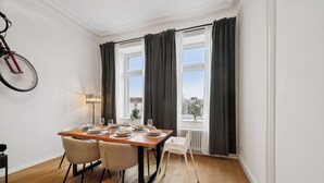 A dining area with a wooden table set for four, two chairs, a bicycle, and a window with curtains.