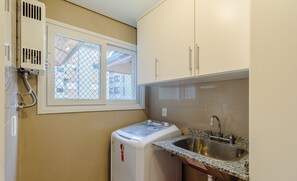 A compact kitchen with a built-in washing machine, a sink, and a window with a view of buildings. - Apt in Canela Facing Duck Lake Cbl307 (Canela)