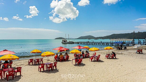 Una playa con sombrillas rojas y amarillas, mesas y sillas.