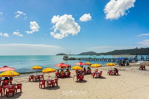 A beach with red and yellow umbrellas, tables, and chairs.