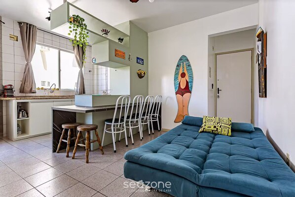 A modern living room with a blue sofa, a dining area with a kitchen counter, and a mural on the wall.