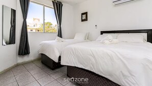 Habitación de hotel con dos camas, un ventanal con cortinas, un equipo de aire acondicionado y un cuadro pequeño en la pared.