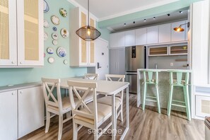 A modern kitchen with white cabinets, a dining table with chairs, and a hanging light fixture.