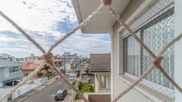 En balkon med udsigt over en boligvej, en parkeret bil og et pigtrådshegn.
