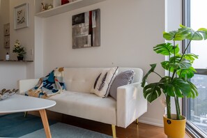 Ein modernes Wohnzimmer mit einem weißen Sofa, einem Couchtisch und einer großen Pflanze in einem gelben Topf.