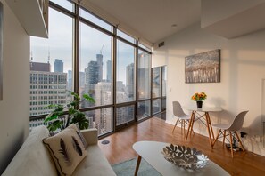 A modern living room with large windows, a sofa, a coffee table, and a dining area with chairs and a small table.