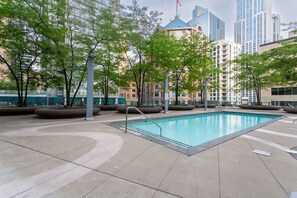 An outdoor swimming pool with a modern design, surrounded by trees and benches, set against a backdrop of high-rise buildings. - Modern 1BR Downtown Toronto | Monthly Rental | Steps to  UT & Financial District (Toronto)