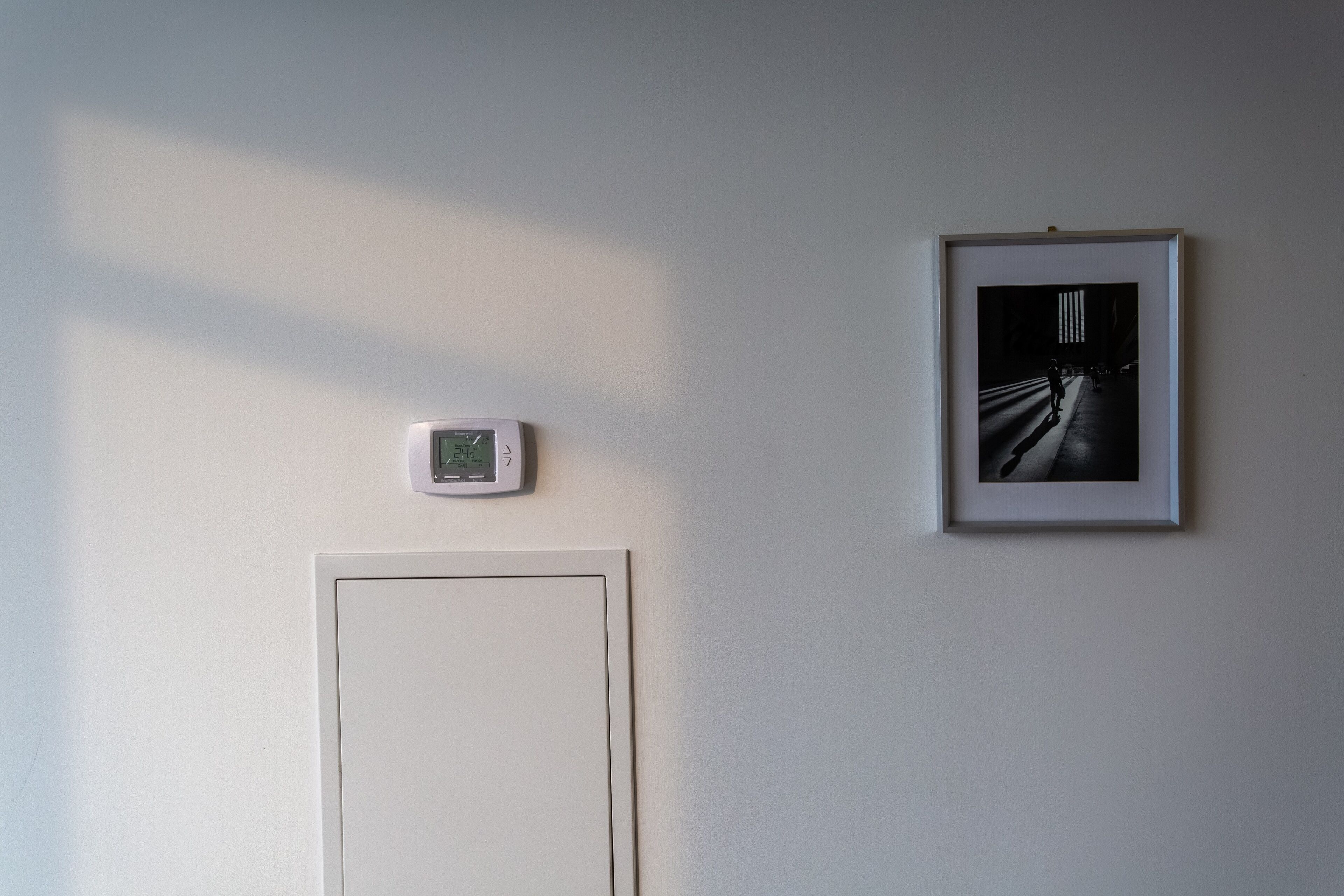 A room with a thermostat, a framed photograph on the wall, and a door.