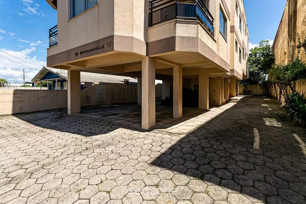Un edificio moderno con un espacio exterior cubierto, pavimentación hexagonal y una señalización de dirección visible.