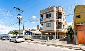 Un edificio de varios pisos con techo plano, un estacionamiento cercado y una calle con coches.