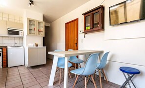 A compact kitchen with a microwave, refrigerator, and cabinets. There is a dining table with four chairs and a blue stool. A wooden door and a small window are visible. - Apart With Barbecue 750 m From the Beach Bou201 (Florianópolis)