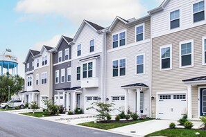 A row of townhouses with white and beige siding, front porches, and a water tower in the background. - Walk to Dtwn! Waterfront 3BR Cambridge Townhome (Cambridge)