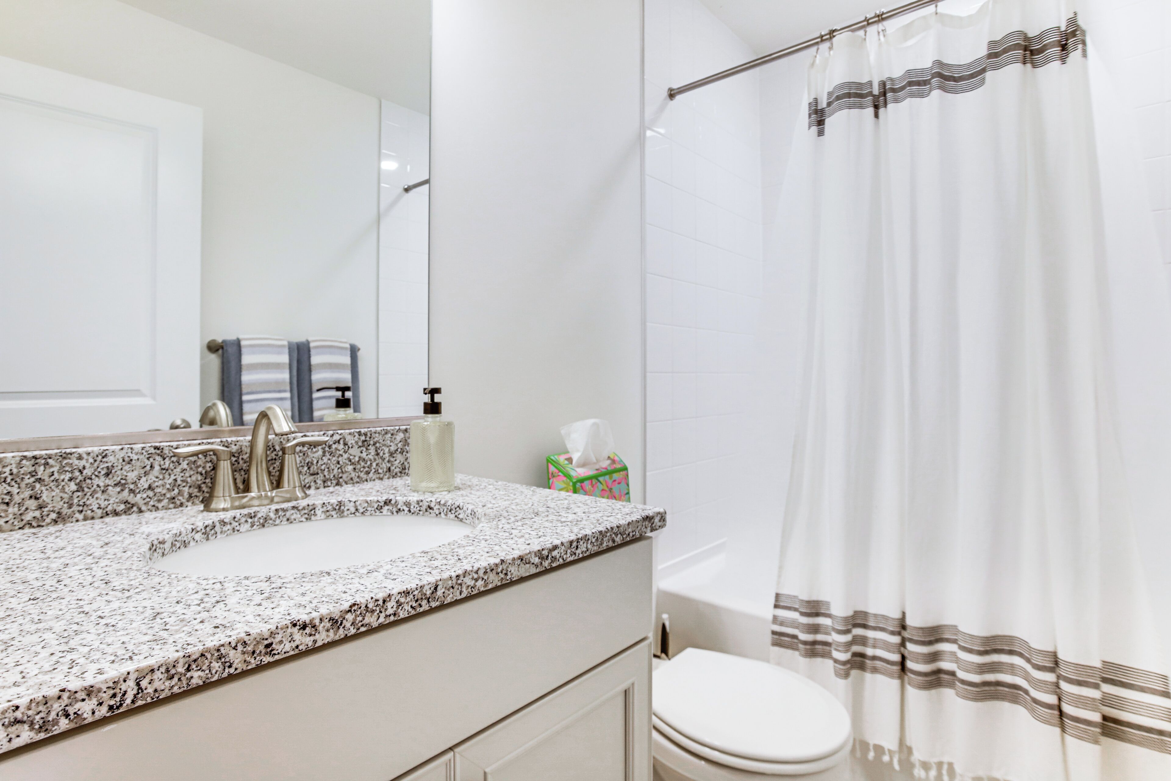 A bathroom with a granite countertop sink, a mirror, a towel rack, a toilet, and a shower curtain.