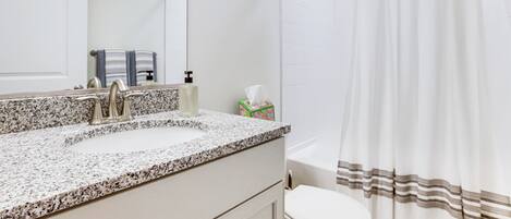 A bathroom with a granite countertop sink, a mirror, a towel rack, a toilet, and a shower curtain.