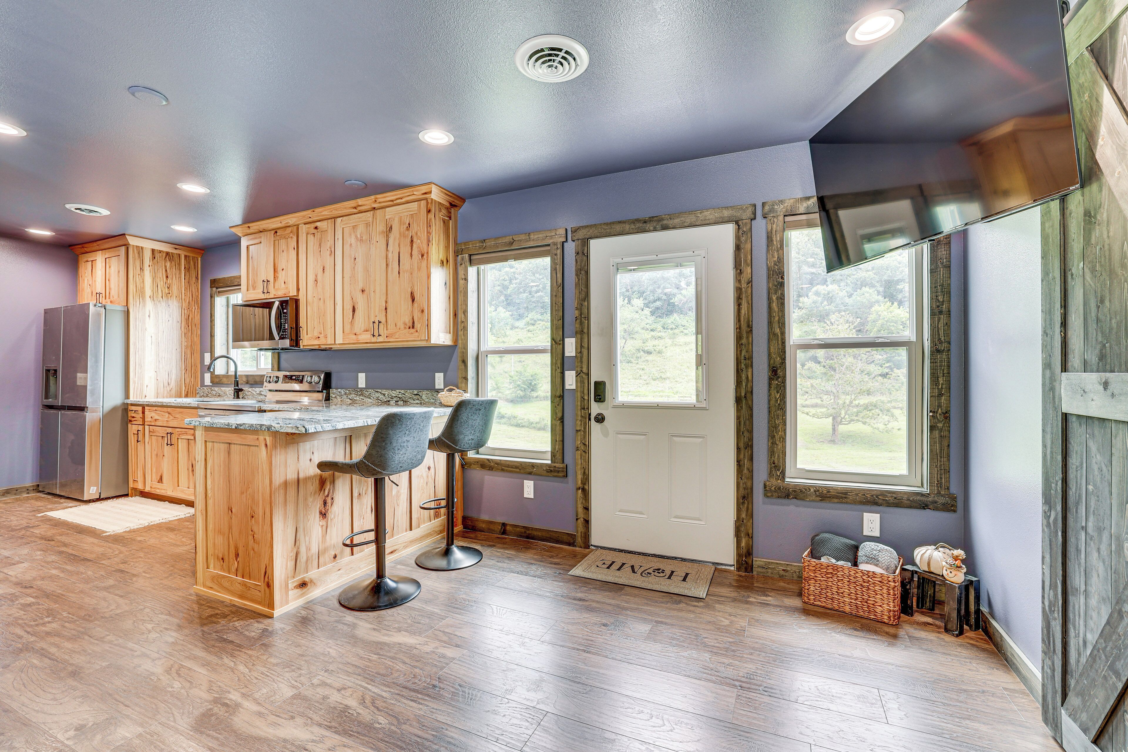 A modern kitchen with wooden cabinets, a central island with bar stools, a refrigerator, and a microwave.