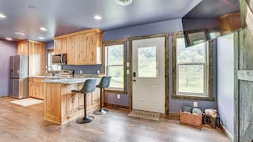 A modern kitchen with wooden cabinets, a central island with bar stools, a refrigerator, and a microwave.