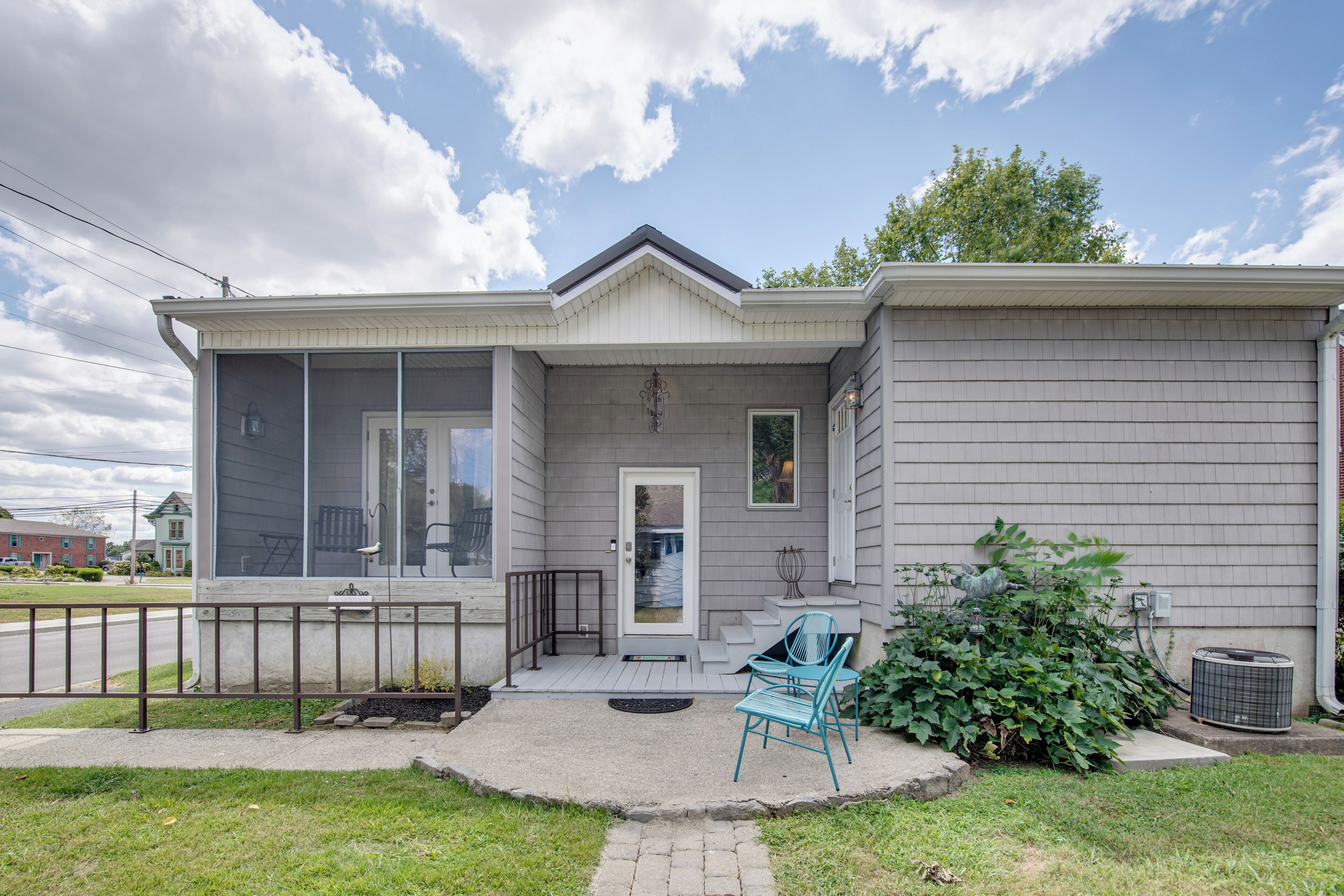 A two-story house with a front porch, a small garden, and a visible air conditioning unit.