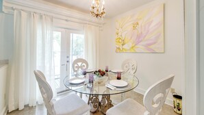 Een eetgedeelte met een glazen tafel, witte gestoffeerde stoelen en een kroonluchter.