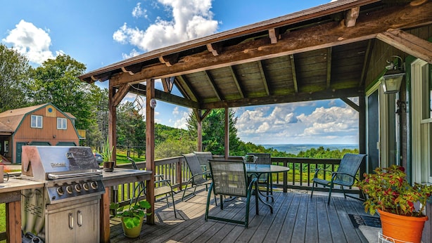A wooden deck with a grill, chairs, and a table. - Pet-Friendly Catskills Home w/ Serene Pond! (Jefferson)