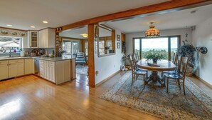 A spacious kitchen with wooden cabinets, a dining area with a round table and chairs, and a view through large windows. - Pet-Friendly Catskills Home w/ Serene Pond! (Jefferson)