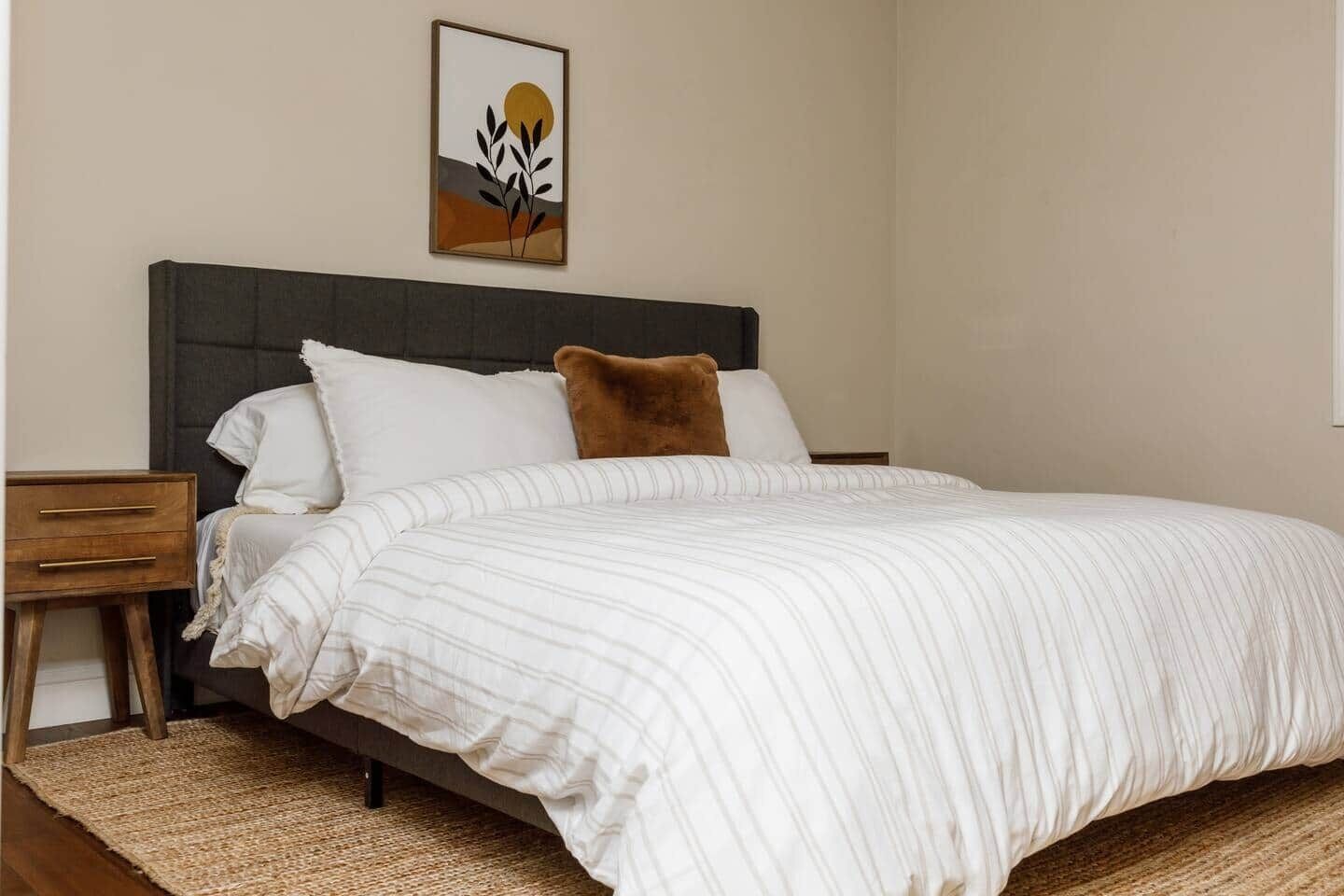 Una cama bien hecha con ropa de cama a rayas, cabecera oscura y una sola almohada.