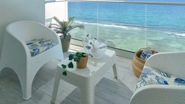 A balcony with white wicker furniture, a hanging light fixture, and a view of the ocean. - Caribbean Sea Breathtaking View Suite (Playa Juan Dolio)