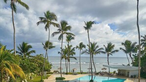 A pool area with clear blue water, surrounded by palm trees and a view of the ocean. - Caribbean Sea Breathtaking View Suite (Playa Juan Dolio)