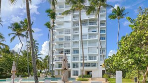 A high-rise hotel with a pool area featuring lounge chairs and palm trees. - Caribbean Sea Breathtaking View Suite (Playa Juan Dolio)
