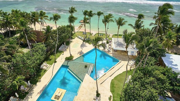A resort with a large swimming pool, palm trees, and a view of the ocean. - Caribbean Ocean View, 2BDRM Beachfront Apartment (Playa Juan Dolio)
