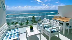 A balcony with a glass barrier, white furniture, and a view of the ocean. - Caribbean Ocean View, 2BDRM Beachfront Apartment (Playa Juan Dolio)
