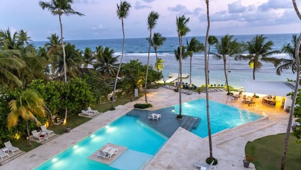 A resort pool area with multiple swimming pools, lounge chairs, and palm trees. - Caribbean Sunscape Beachfront Apartment (Playa Juan Dolio)