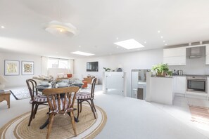 A modern kitchen with white cabinets, a built-in oven, and a dining area with a round table and chairs.