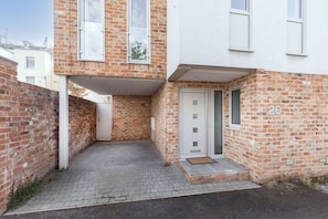 A two-story brick building with a small paved courtyard, a white door, and a mailbox. - Contemporary 2-Bed 2-Bath Home with Parking (Gloucestershire)