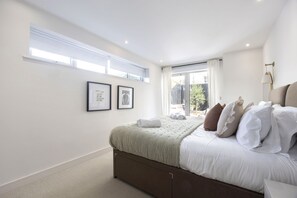 A bedroom with a bed, a window, and a wall-mounted lamp. - Contemporary 2-Bed 2-Bath Home with Parking (Gloucestershire)