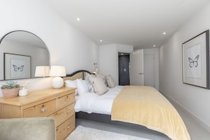 Une chambre à coucher comprenant un lit, une commode, un miroir et des œuvres d’art encadrées accrochées aux murs.