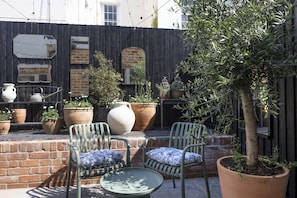 Un patio con dos sillas, una mesa, plantas en macetas y un árbol.