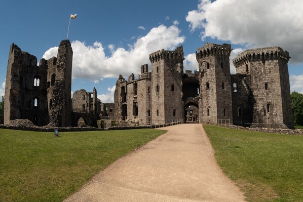 An ancient castle with a flag on top of a tower, surrounded by grassy areas and a clear sky.