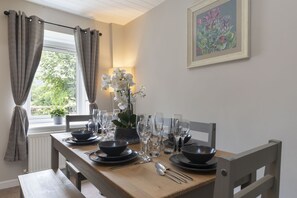 Ein Esstisch ist gedeckt mit Schüsseln, Tellern, Besteck und Gläsern. Auf der Wand hängt ein gerahmtes Blumenbild, und eine Orchidee steht in einem Topf darauf.