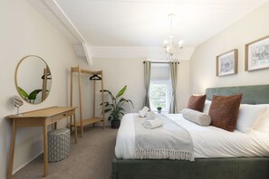 A bedroom with a bed, bedside table, mirror, hanging clothes rack, potted plant, and a window with curtains.