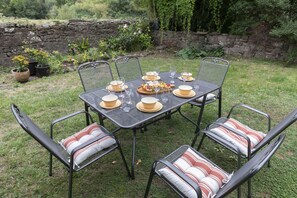 Un espace de restauration en plein air avec une table et des chaises en métal, entouré d’un mur de pierre et de verdure.