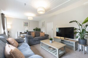 Un salon moderne avec un canapé gris, une table basse, un téléviseur et une plante en pot.