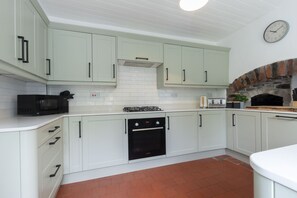 Una cocina con armarios blancos, un horno negro, microondas y chimenea de ladrillo.