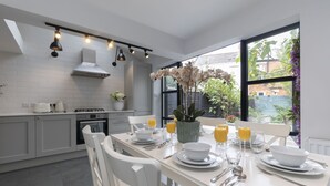 A modern kitchen with white cabinets, a dining table set for breakfast, and a large window with a view of greenery. - Jing House - A Beautiful Two Bedroom Home (Gloucestershire)