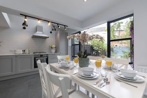 A modern kitchen with white cabinets, a dining table set for breakfast, and a large window with a view of greenery.