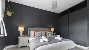 A modern bedroom with a large bed, two bedside tables, and a dark-colored wardrobe. - Jing House - A Beautiful Two Bedroom Home (Gloucestershire)