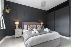 A modern bedroom with a large bed, two bedside tables, and a dark-colored wardrobe.