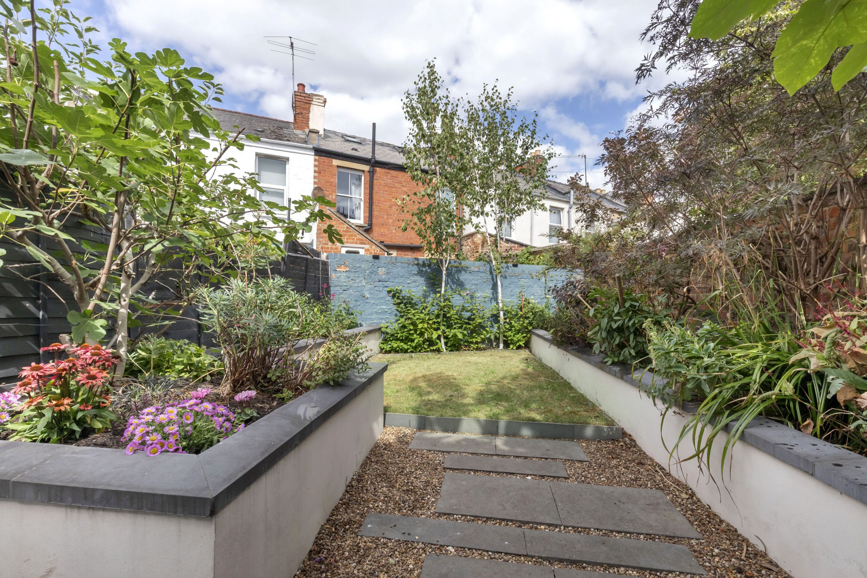 A garden pathway leading to a grassy area with a brick wall and various plants.