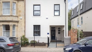 A two-story residential building with a white facade, two visible windows, and a black metal fence in front. - Jing House - A Beautiful Two Bedroom Home (Gloucestershire)