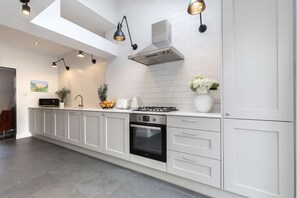 A modern kitchen with white cabinetry, a built-in oven, a stainless steel range hood, and pendant lighting.