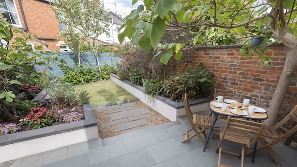 A patio with a table and chairs, surrounded by a brick wall and plants. - Jing House - A Beautiful Two Bedroom Home (Gloucestershire)